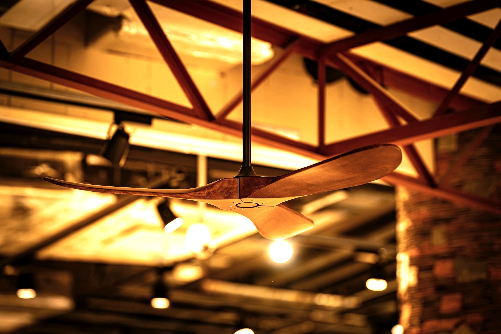 Wooden-blade ceiling fan in restaurant with exposed red beams and brick